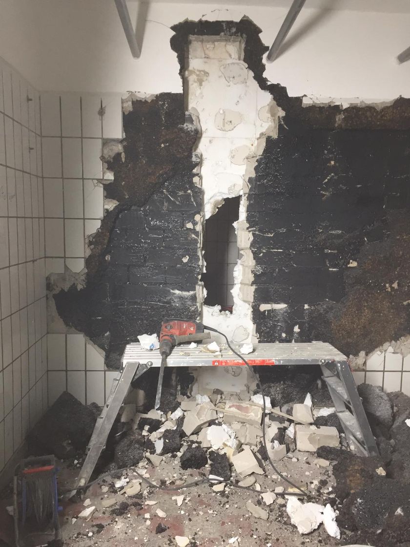 Abgestemmte Fliesenwand mit freigelegtem, schwarz beschichtetem Mauerwerk und Bauschutt am Boden